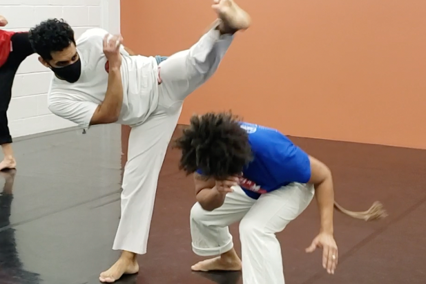 Capoeira Camará student throws a martelo while Professor Chaveco esquivas under the kick